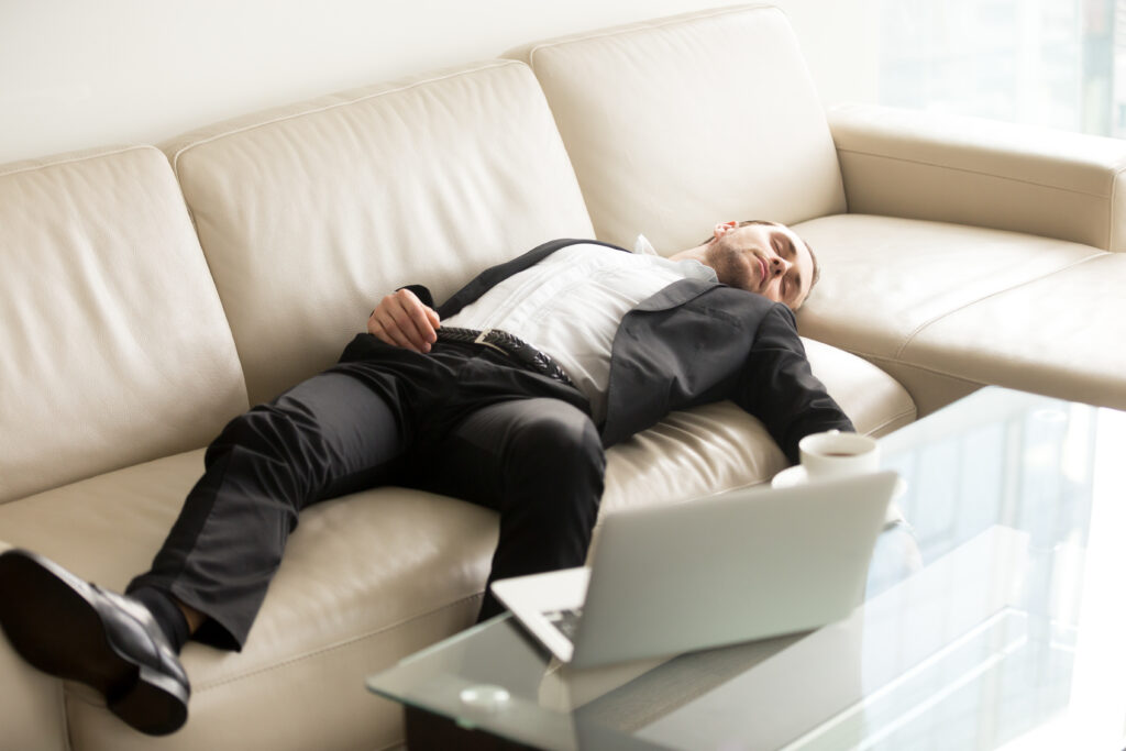 Tired businessman lying relaxed on sofa. Man fall asleep on couch in office when stayed at work till late. Entrepreneur takes short break, recovery sleep after too much hard work at project on laptop